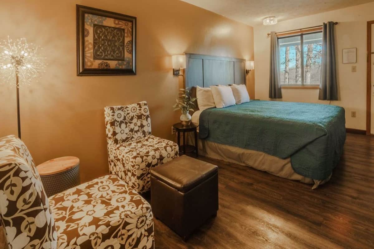 A cozy room with a bed, a chair, a small table, and a lamp.