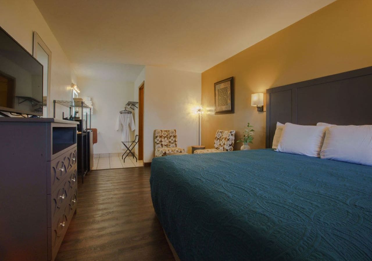 Una habitación de hotel con una cama grande, un aparador, una silla, una lámpara y una televisión.