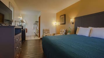 Una habitación de hotel con una cama grande, un aparador, una silla, una lámpara y una televisión.