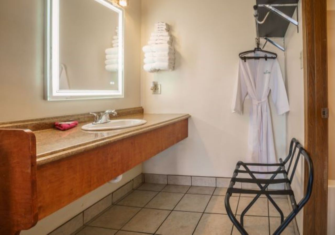 A bathroom with a wooden vanity, a large mirror, a towel rack, and a black chair.