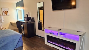 A hotel room with a bed, a desk with a computer, a TV, and a fireplace. - Shady Acre Inn and Suites (Branson West)