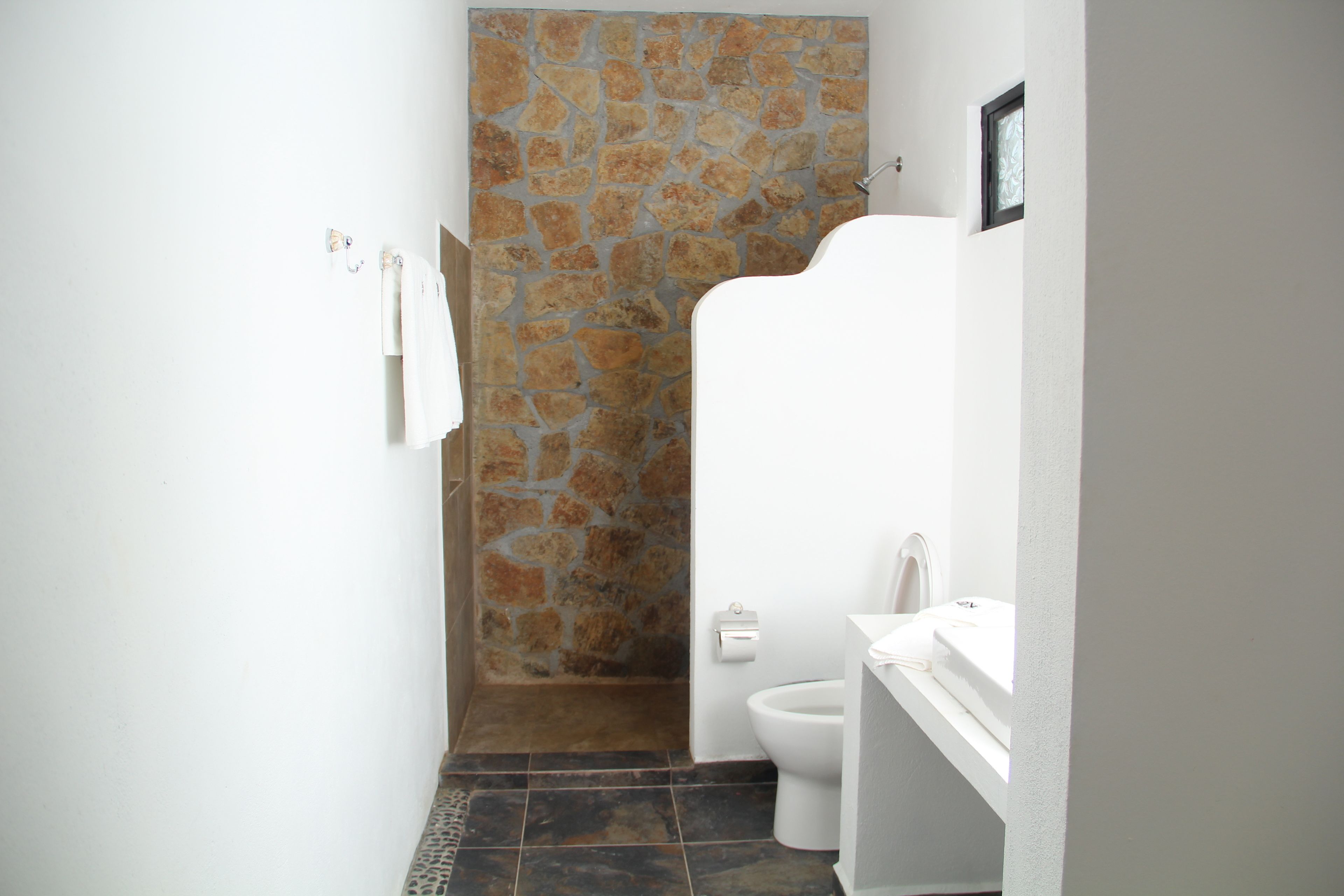 A bathroom with a stone shower wall, a toilet, and a sink.