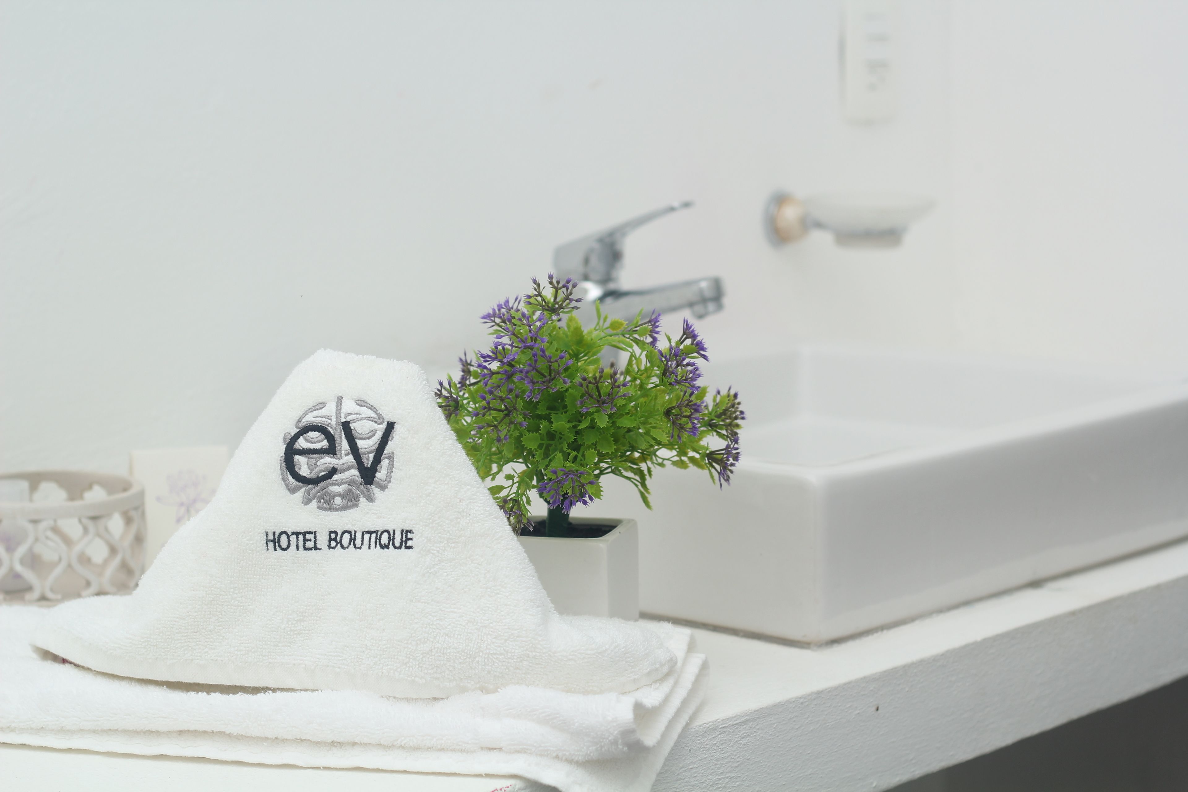 A white towel with "ev HOTEL BOUTIQUE" text, a small potted plant, and a white sink in a bathroom.