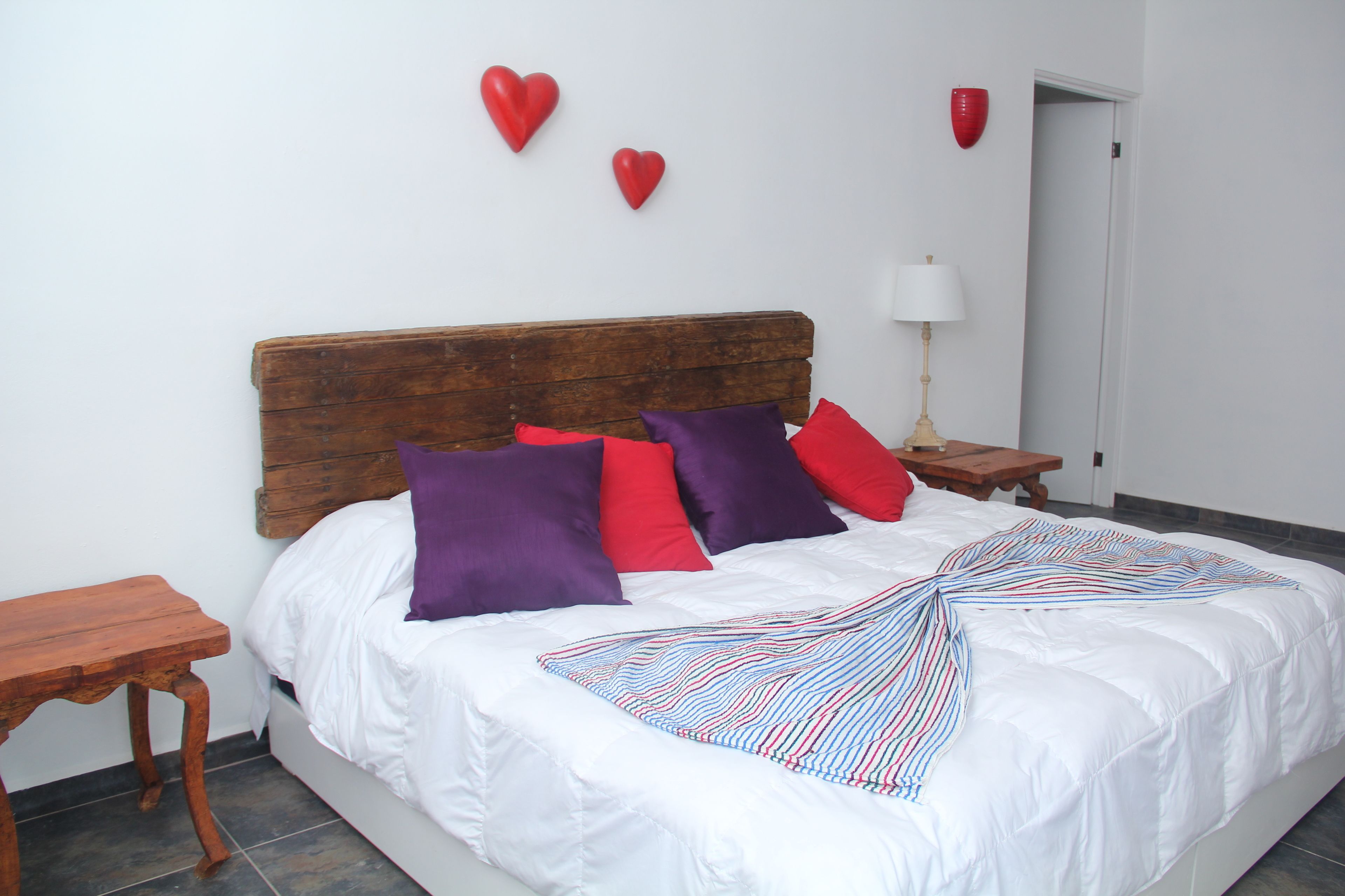 A bed with white bedding, a wooden headboard, and multiple pillows in red and purple.