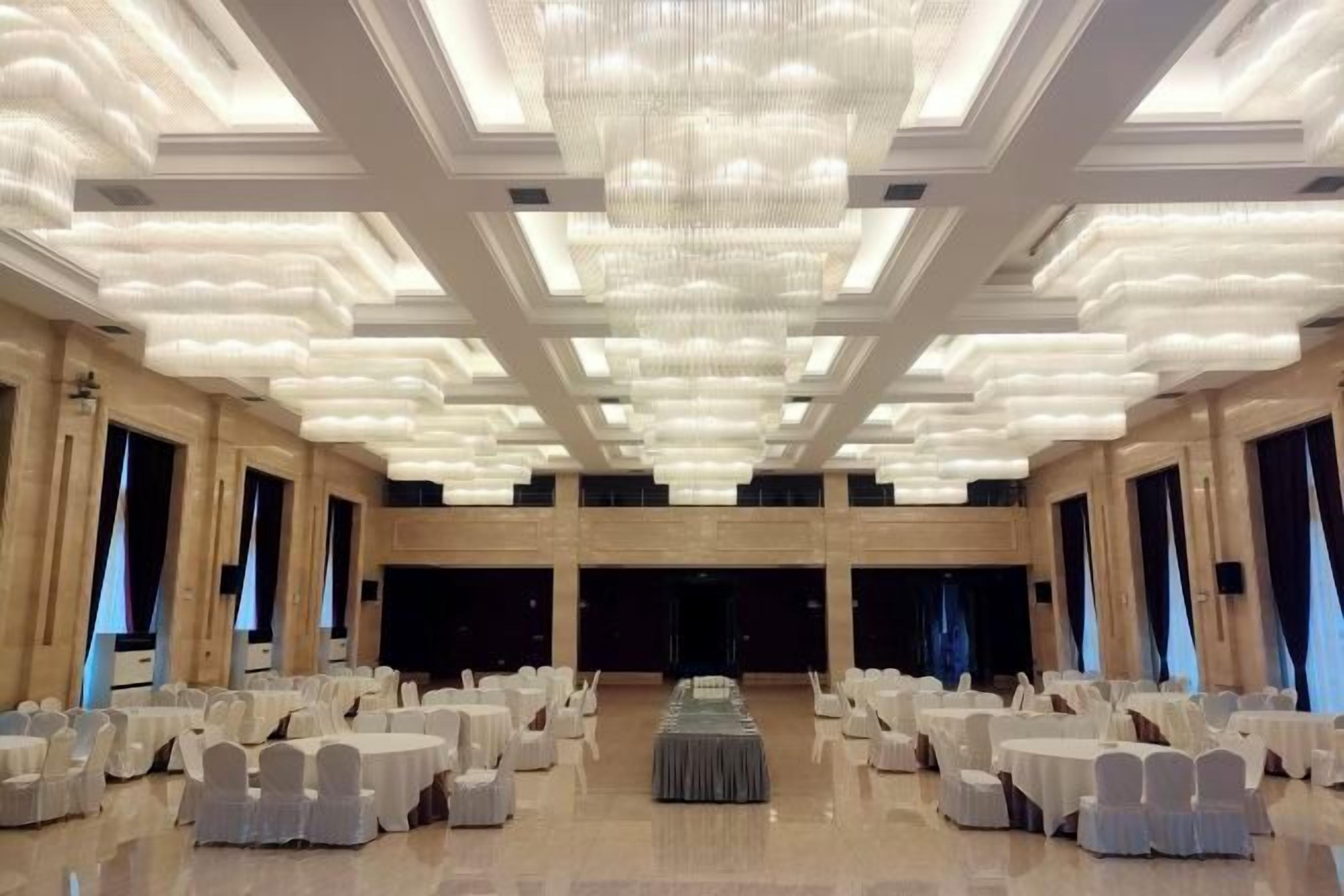 A banquet hall with rows of round tables, a central stage, and a large chandelier.