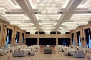 Un salón de banquetes con filas de mesas redondas, un escenario central y una gran lámpara de araña.