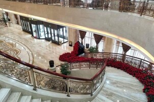 Un amplio vestíbulo de hotel con piso de mármol, una escalera curva y una barandilla decorativa.