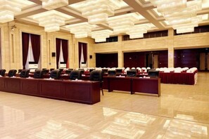 Un salón de conferencias con varias mesas y sillas, un piso de madera pulida y un techo alto con lámparas colgantes.