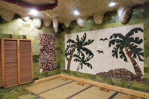 A room with a tiled floor, a wooden bench, a wall with a palm tree mural, and a patterned wall. - Mengguzhen Hotel (Fuxin)