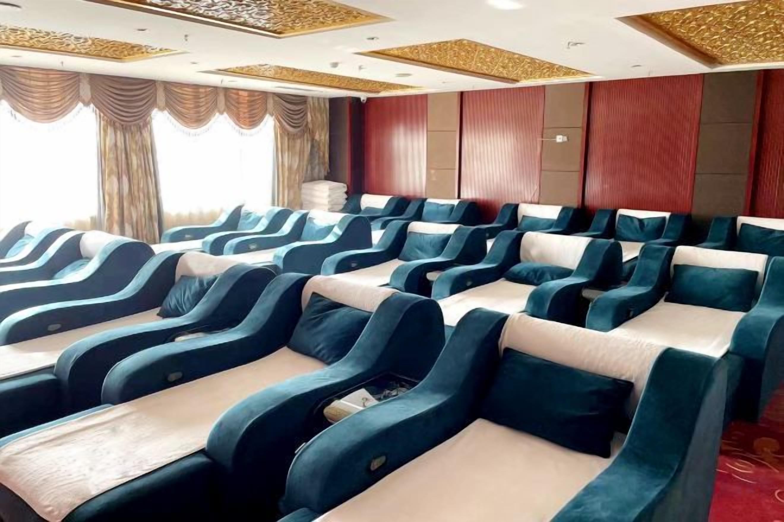 A row of reclining massage chairs in a room with a patterned ceiling and a view of the outdoors.