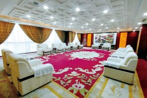 Habitación de hotel con una alfombra roja grande, sofás blancos e iluminación empotrada en el techo.