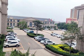 A parking lot with multiple cars, a building with a large entrance, and a clear sky. - Mengguzhen Hotel (Fuxin)
