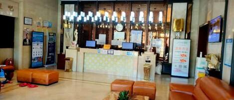 A hotel lobby with a reception desk, seating area, and a decorative wall.
