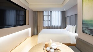 Une chambre d’hôtel moderne avec un grand lit, une table de chevet avec un service à thé et une grande fenêtre avec des rideaux.