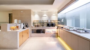 Une cuisine moderne dotée d’un espace dédié au café, d’un buffet proposant divers plats et d’une grande fenêtre laissant entrer la lumière naturelle.