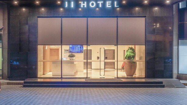 L’extérieur de l’hôtel Ji présente une façade moderne, une grande entrée vitrée et un écran numérique au-dessus des portes.