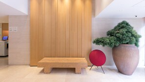 Un espace d’accueil avec un banc en bois, une grande plante en pot et une chaise rouge.