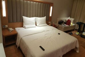 Habitación de hotel con una cama grande, un cabecero, una mesita de noche con un teléfono y un sofá con equipaje.