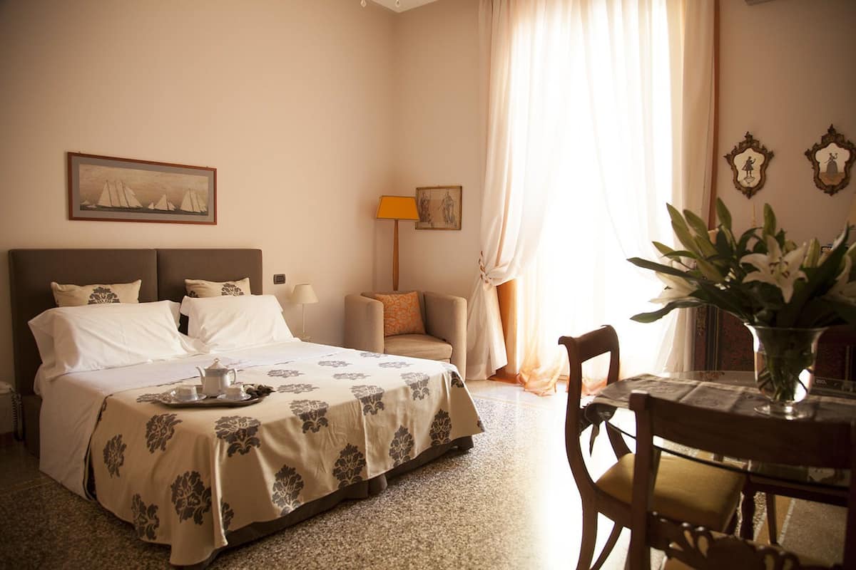 A hotel room with a bed, a table with a vase of flowers, and a chair.