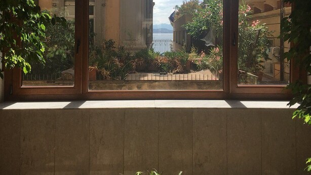 A view through a window with a balcony, overlooking a street with buildings and a body of water.