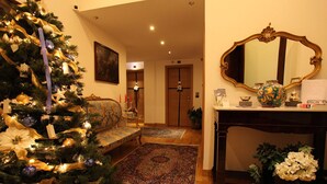 A warmly lit room with a Christmas tree, a sofa, a console table with a mirror, and a door leading to another room.