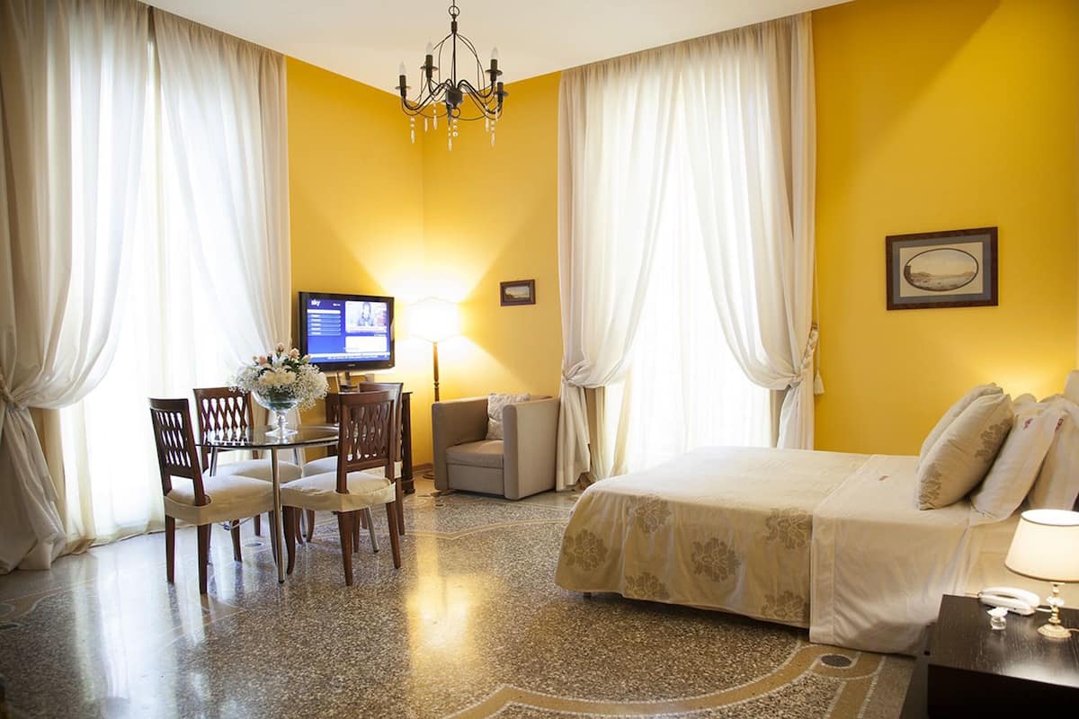 A hotel room with a bed, a desk with a computer, a chair, and a sofa.