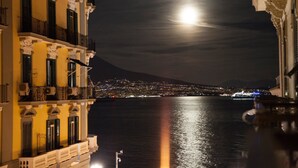 A night view of a coastal city with a prominent mountain in the background, illuminated buildings along the waterfront, and a large ship docked at the harbor.