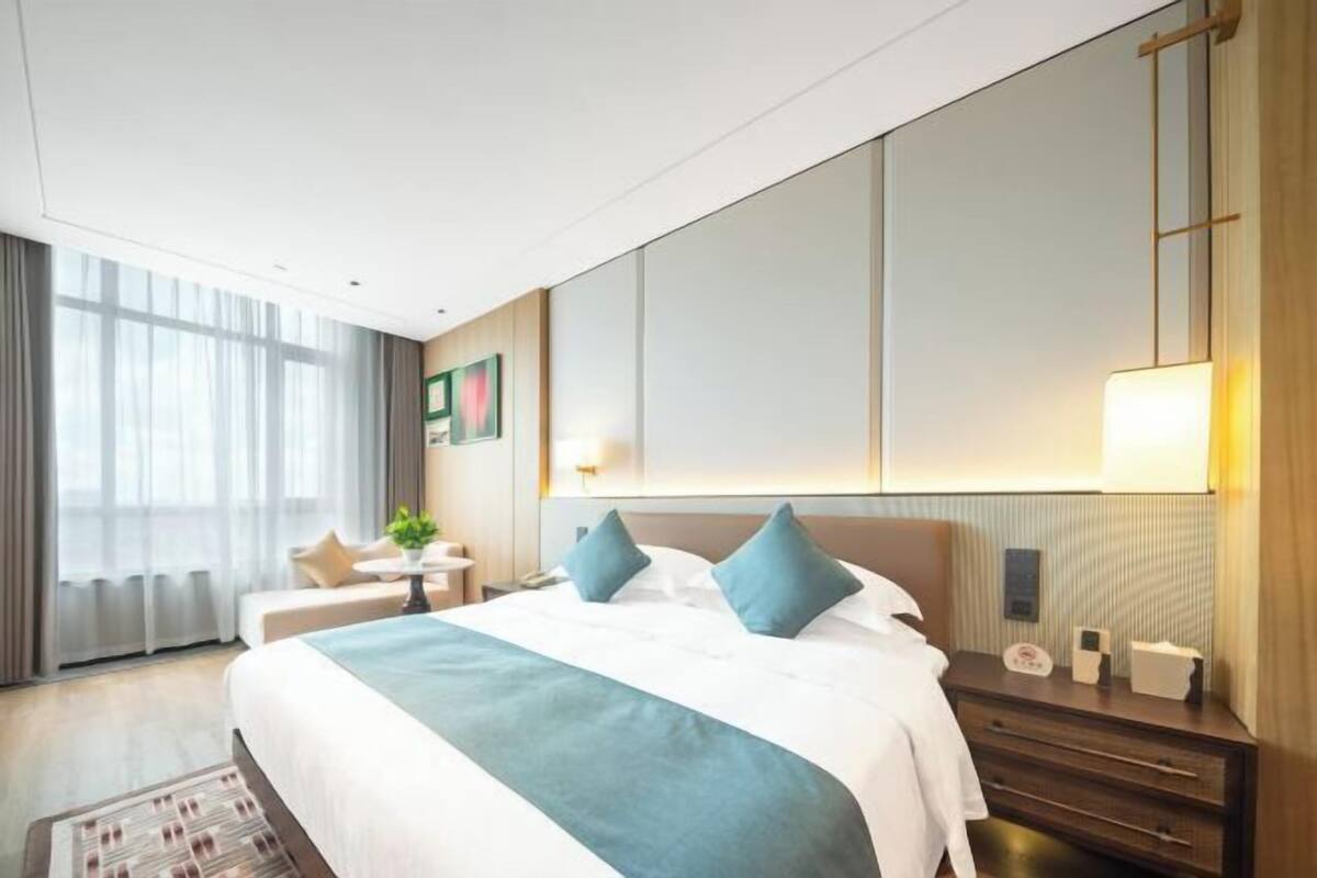 A hotel room with a large bed, bedside tables, a desk, and a window with curtains.