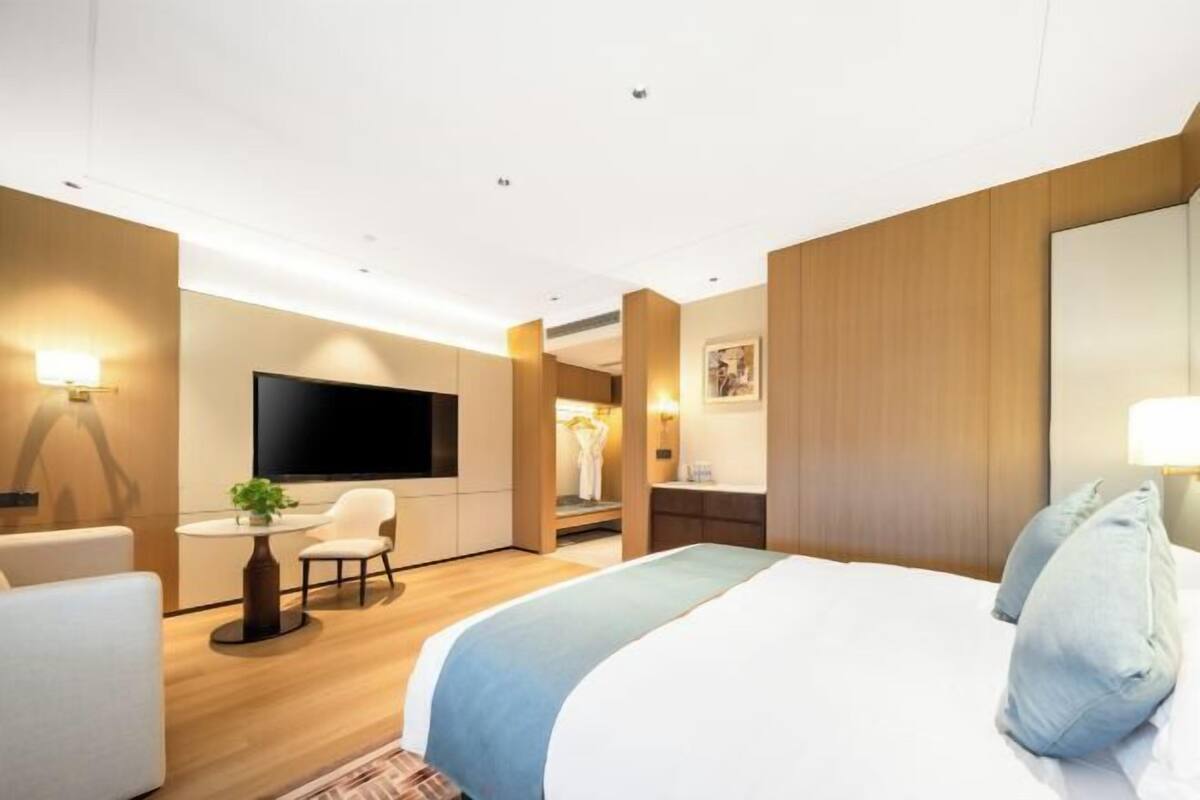 A modern hotel room with a bed, a desk, a chair, a TV, and a mirror.