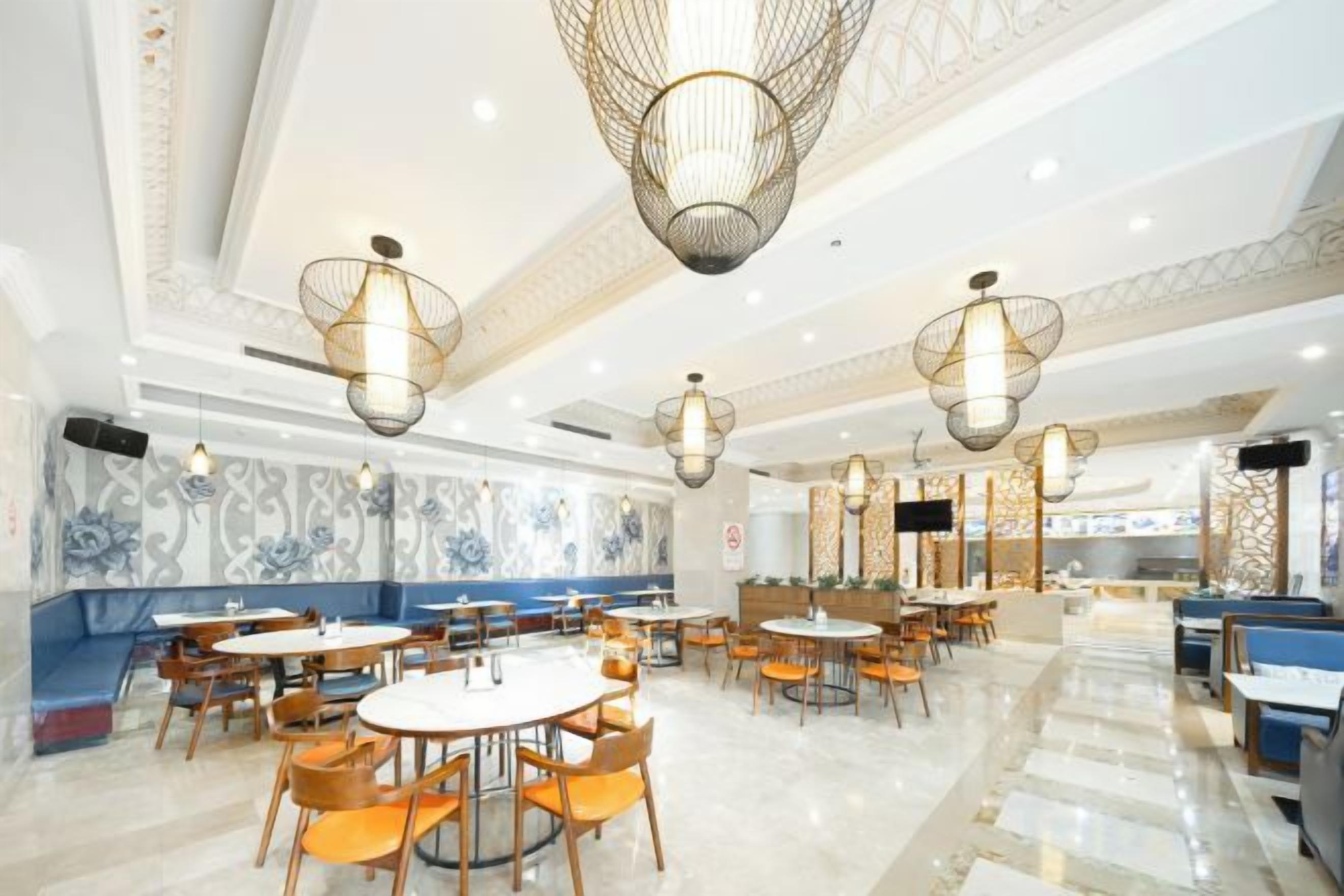 A spacious dining area with round tables and chairs, decorative ceiling lights, and patterned wall designs.