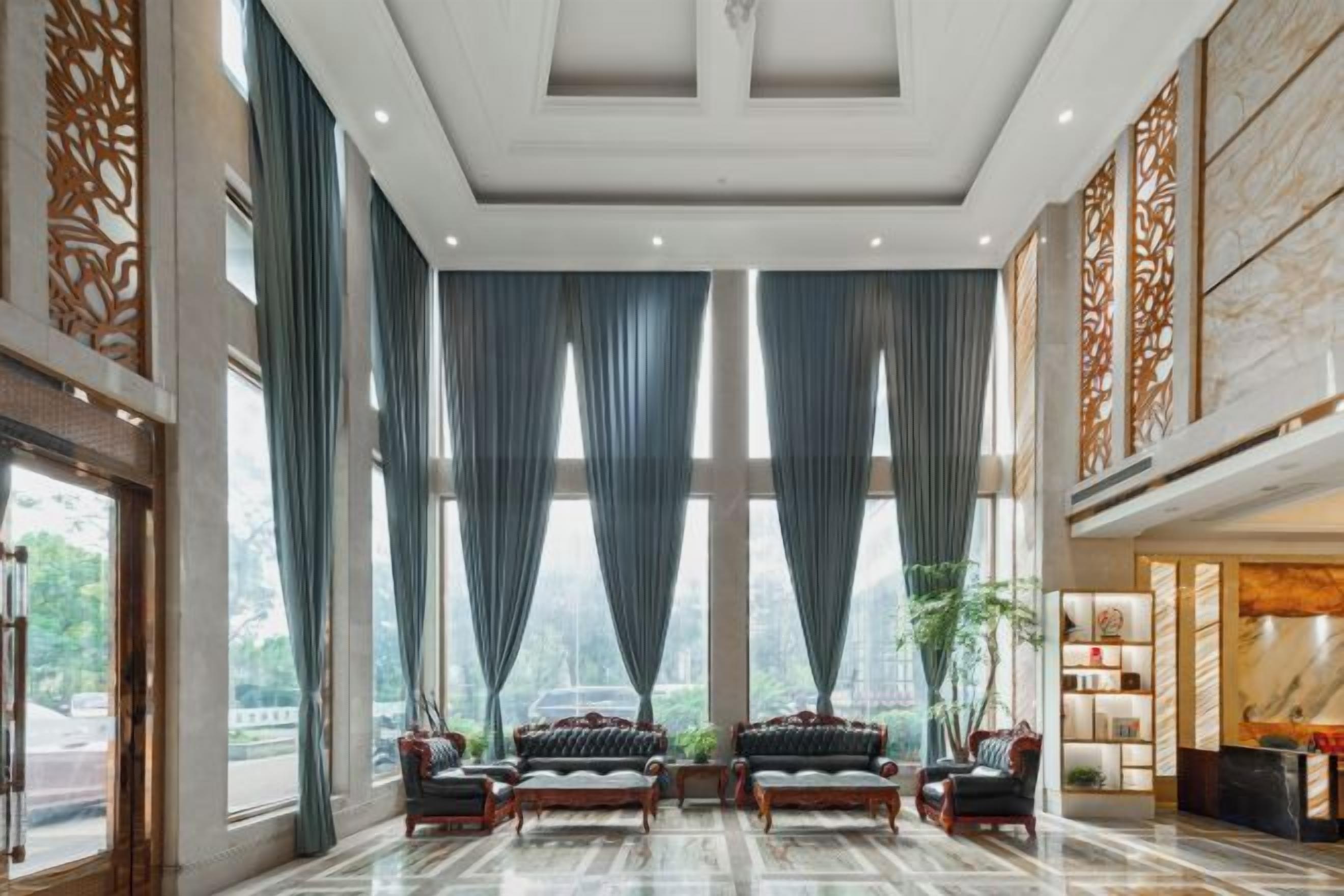 A spacious lobby with a high ceiling, large windows with curtains, and a seating area with sofas and chairs.