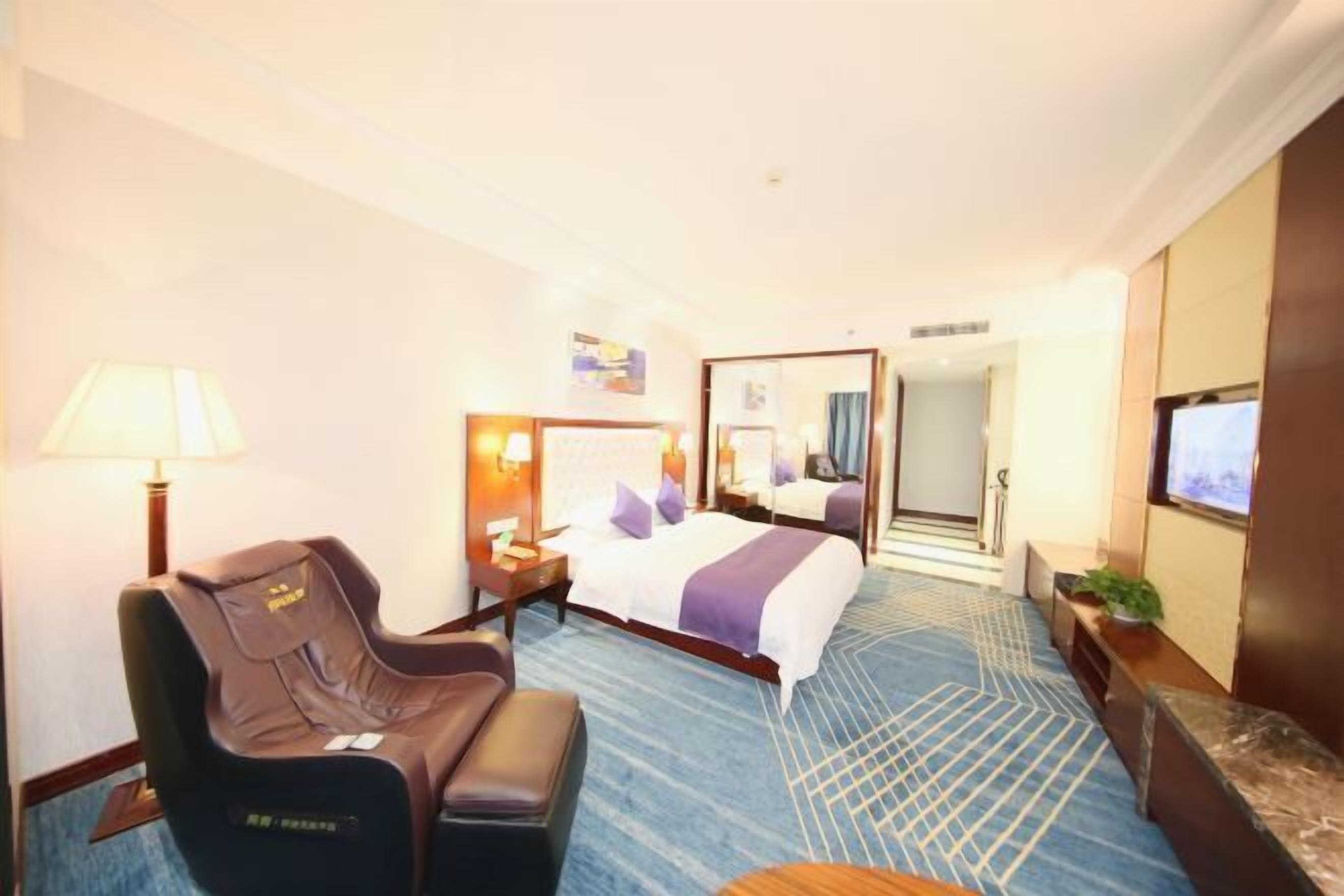 Ett hotellrum med en säng, en massagefåtölj, ett skrivbord och en TV.