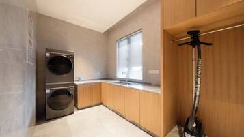 A compact kitchen with a double washing machine, a sink, and a wine bottle on the counter.