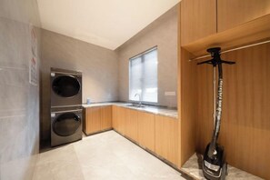 A compact kitchen with a double washing machine, a sink, and a wine bottle on the counter. - Huhua International Hotel (Shanghai Wujing Hua Normal University Branch) (Shanghai)