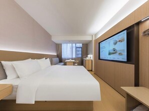 A hotel room with a large bed, a TV mounted on the wall, a bedside table, and a small desk with a chair.