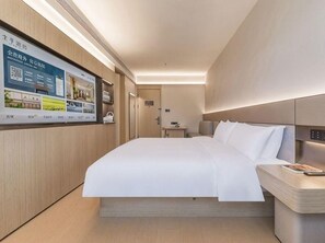 A modern hotel room with a large bed, a bedside table, a wall-mounted TV, and a wooden floor.