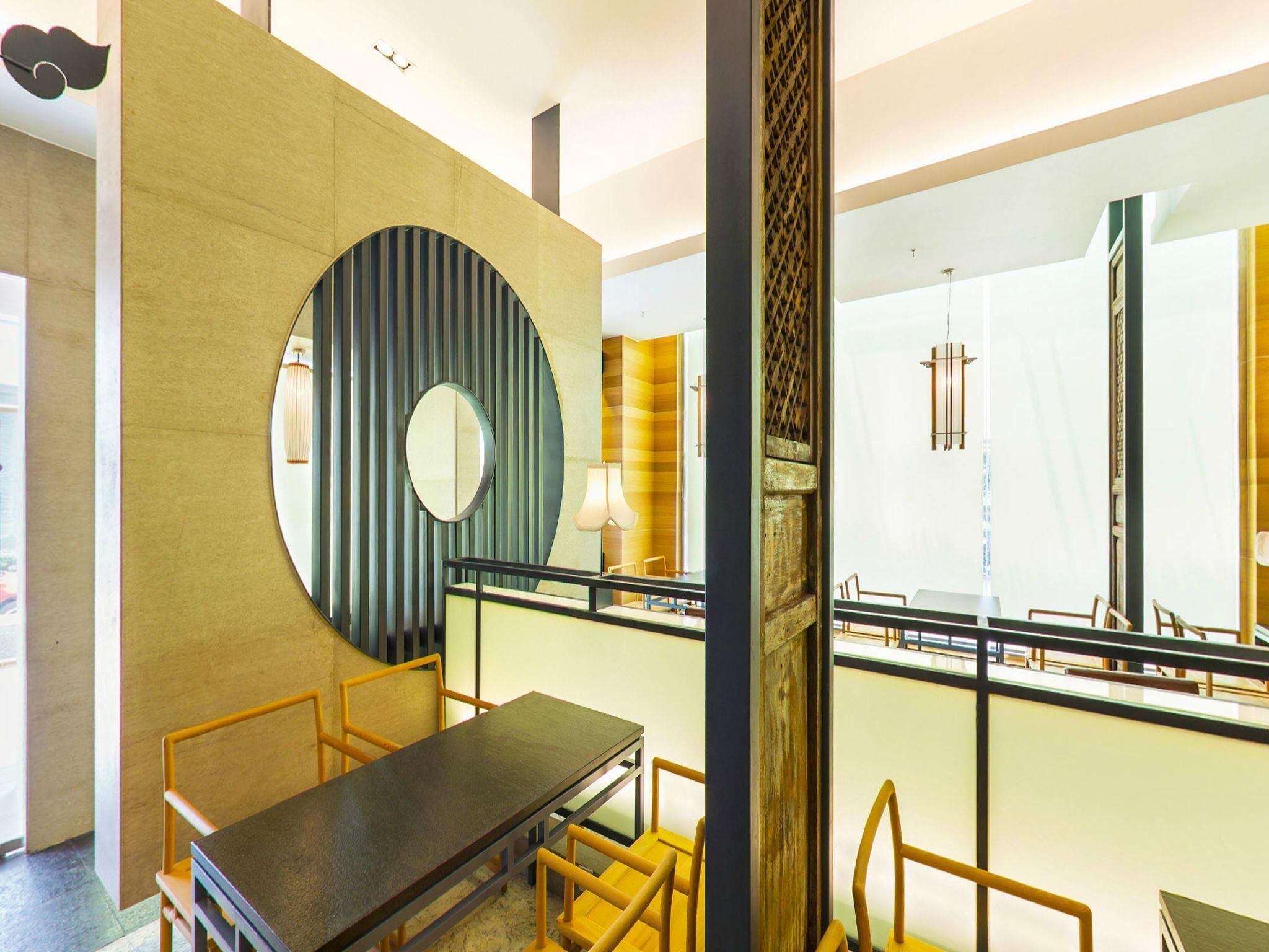 A modern interior with a dining area, a large circular mirror, and a staircase.