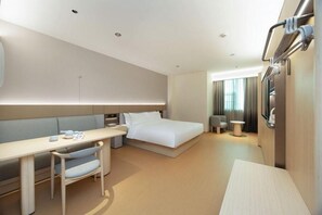 A modern hotel room with a bed, a desk, a chair, a bedside table, and a television.