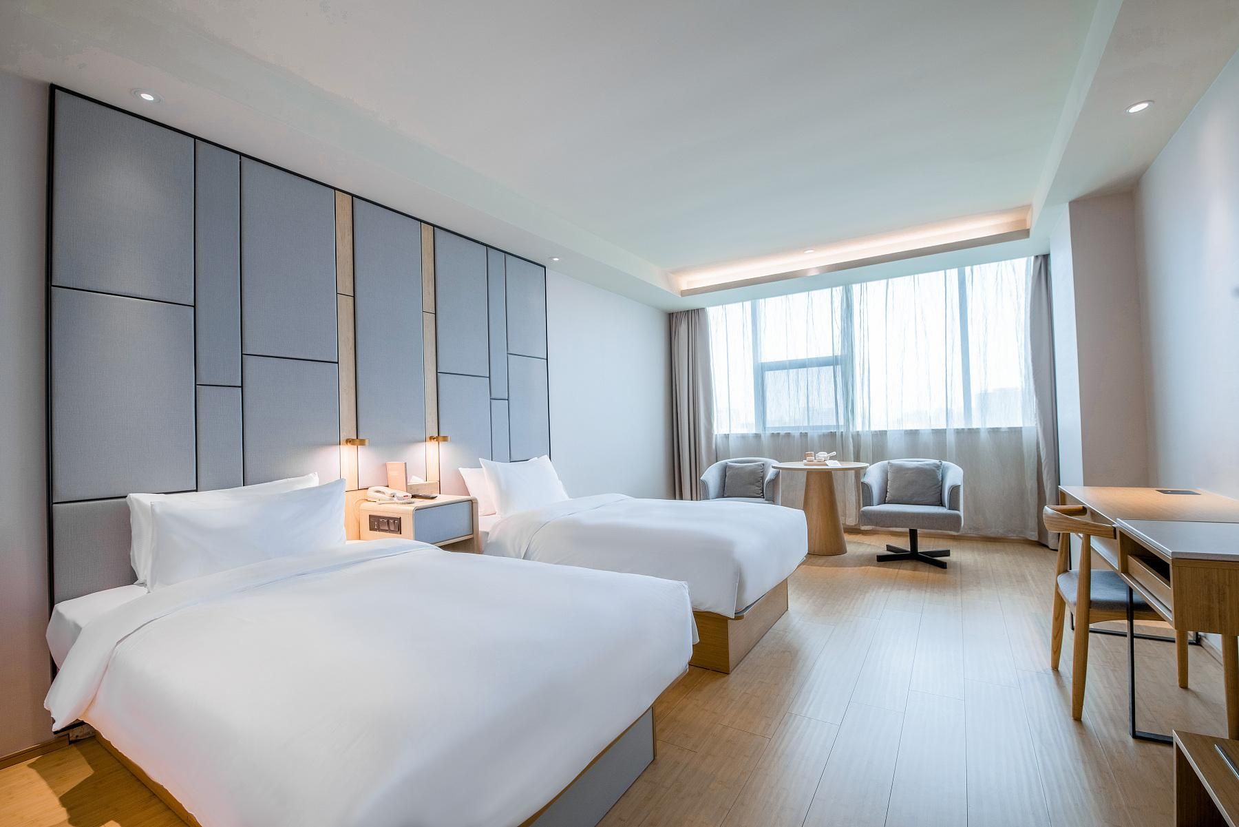 A hotel room with two beds, a desk, a chair, and a large window.