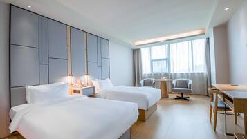 A hotel room with two beds, a desk, a chair, and a large window.