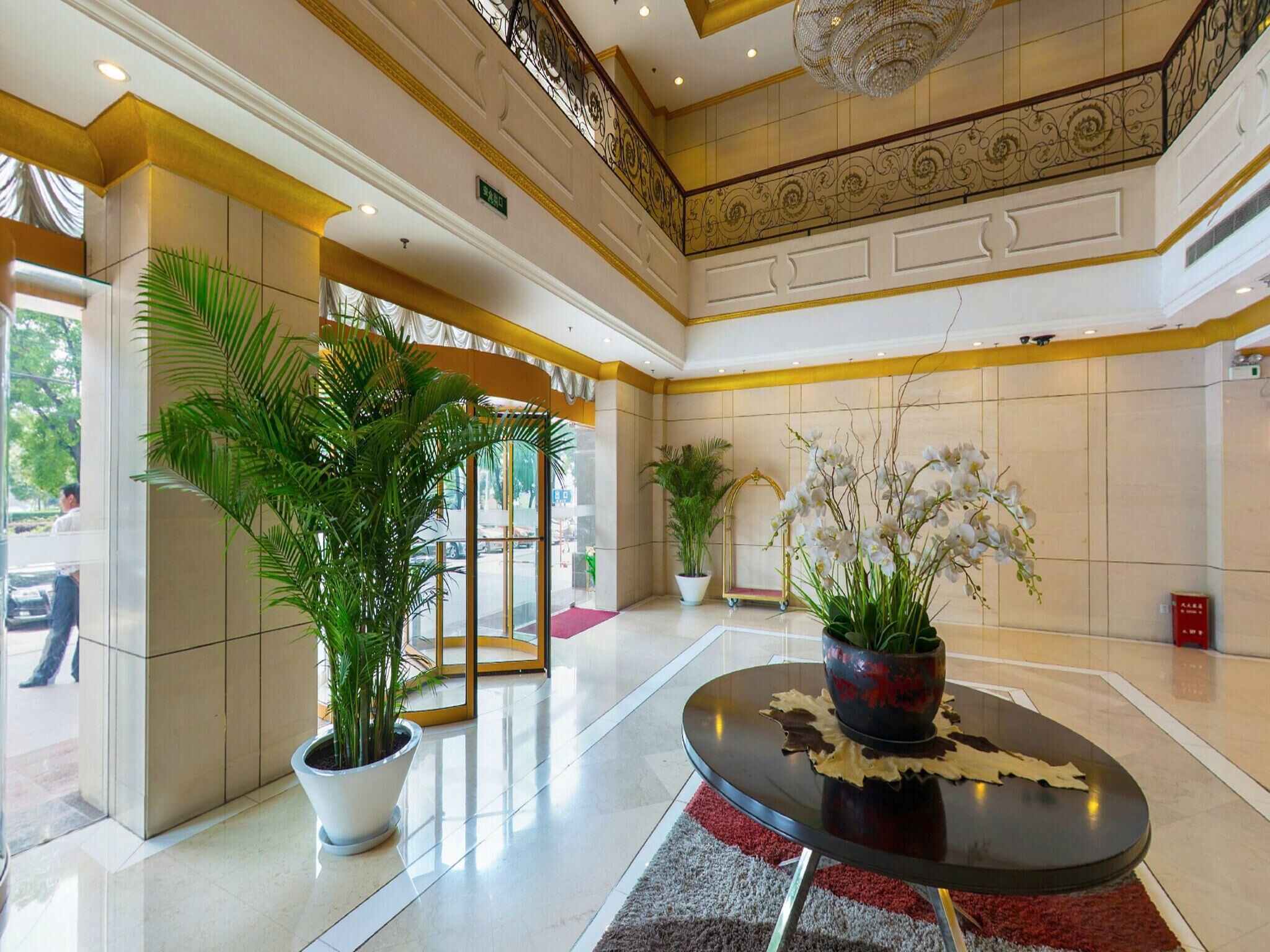 A lobby with a glass door entrance, potted plants, a round table with a decorative centerpiece, and a chandelier.