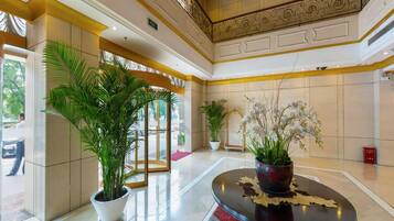 A lobby with a glass door entrance, potted plants, a round table with a decorative centerpiece, and a chandelier.