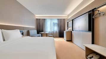A modern hotel room with a large bed, a desk, a chair, a wardrobe, and a shoe rack.