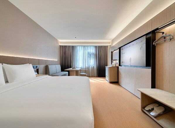 A modern hotel room with a large bed, a desk, a chair, a wardrobe, and a shoe rack.