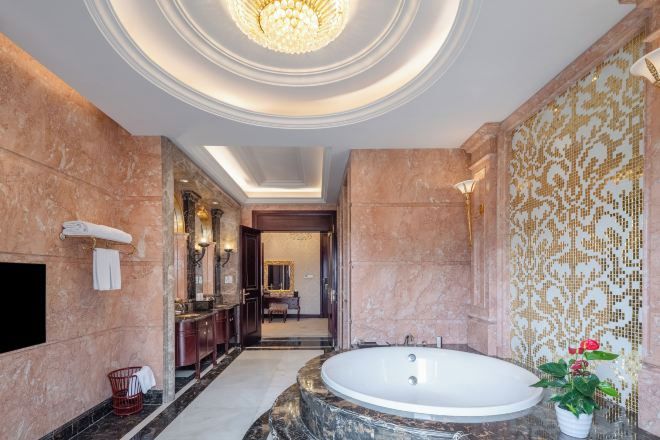 A luxurious bathroom with a large freestanding bathtub, marble walls, and a chandelier.