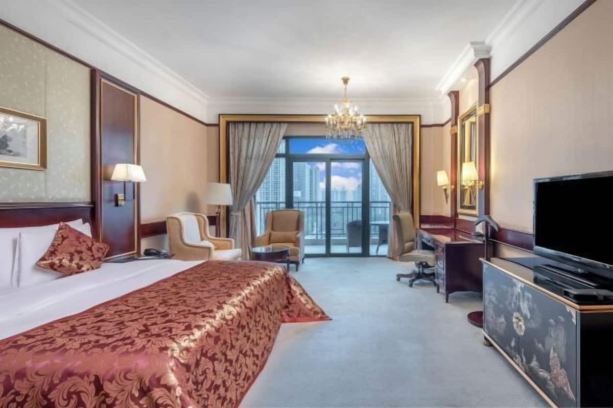 A hotel room with a large bed, a desk, a TV, and a view of the city.