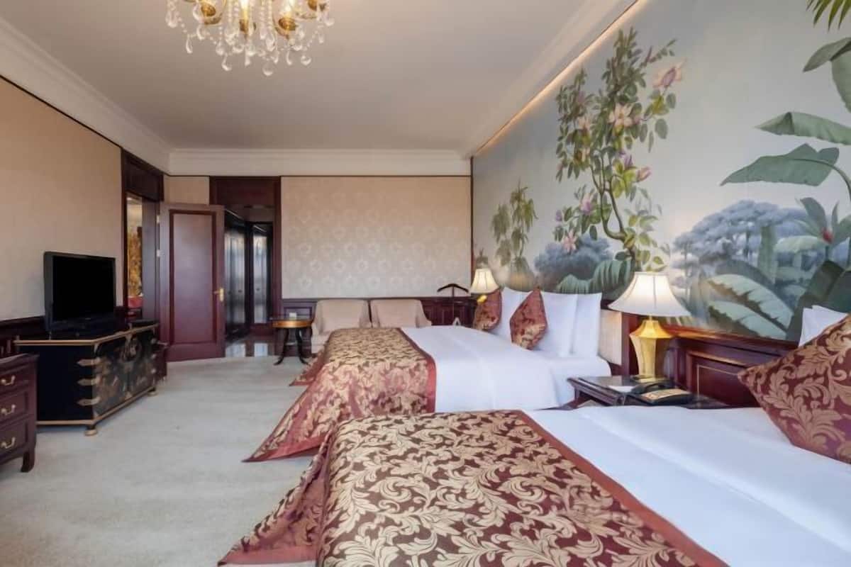 A hotel room with two beds, a television, a chandelier, and a mural of foliage on the wall.