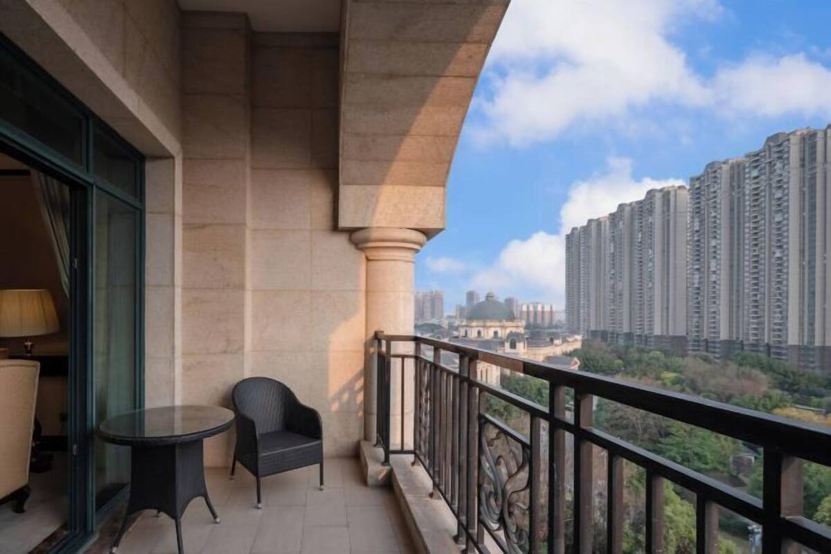 A balcony with a table and chair, overlooking high-rise buildings and greenery.
