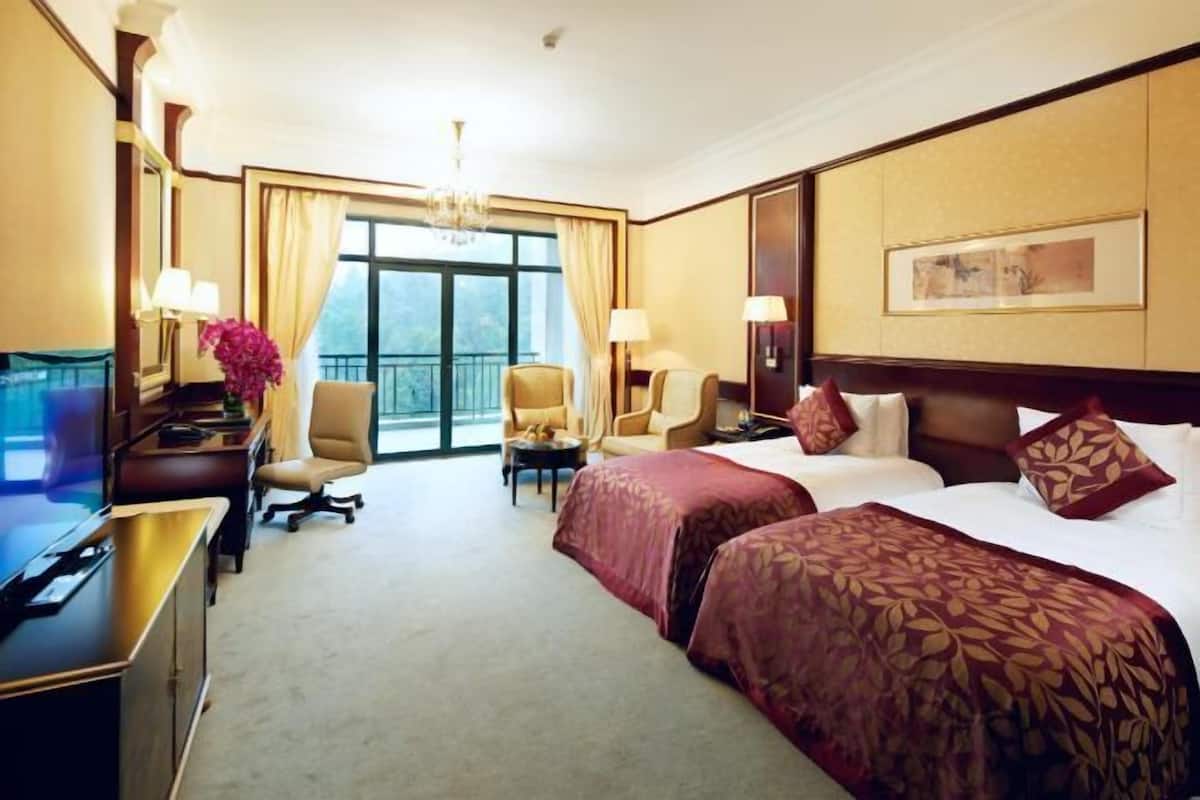 A hotel room with a large bed, two armchairs, a desk, a TV, and a window with curtains.