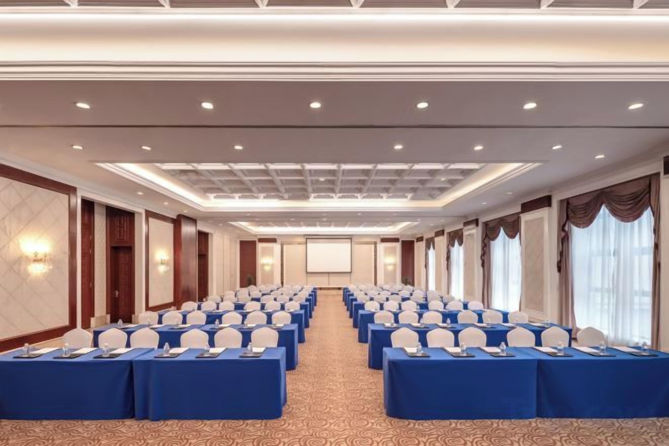 A conference room with rows of tables, each with a blue tablecloth and white chairs, equipped with nameplates.